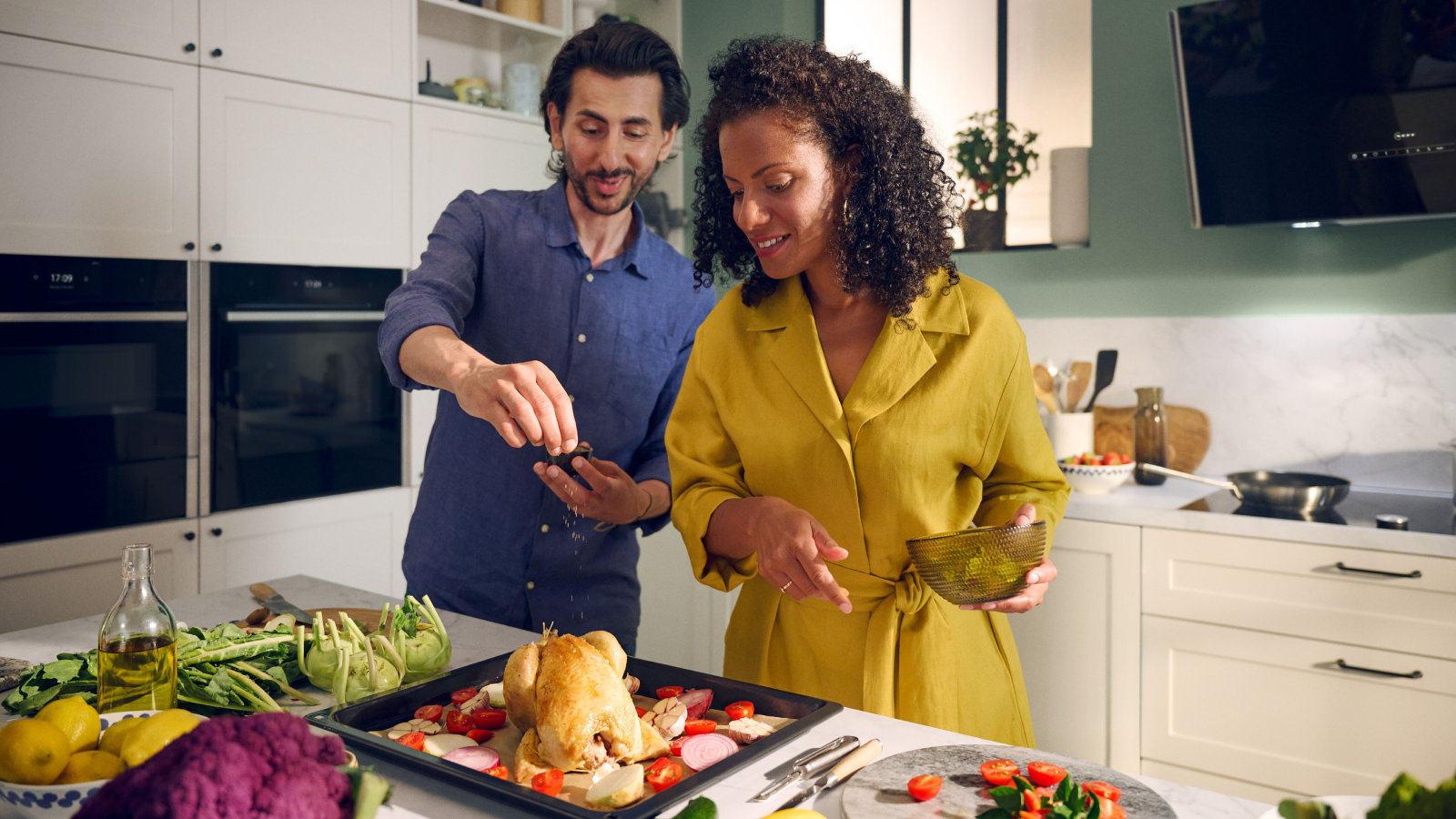 A couple preparing a roast chicken together with two NEFF ovens in the background.